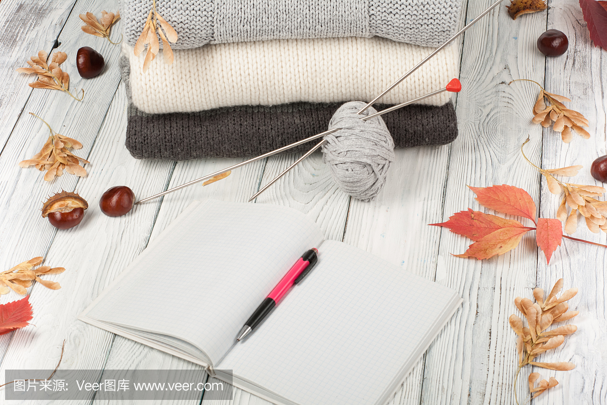 针织羊毛毛衣。木色背景的针织冬装、秋装、毛衣、针织品、笔、书、文字空间
